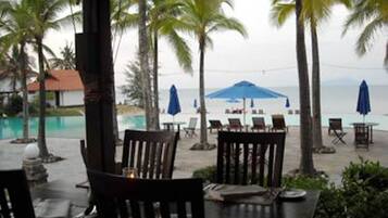 An outdoor seating area with tables and chairs, overlooking a pool and palm trees.