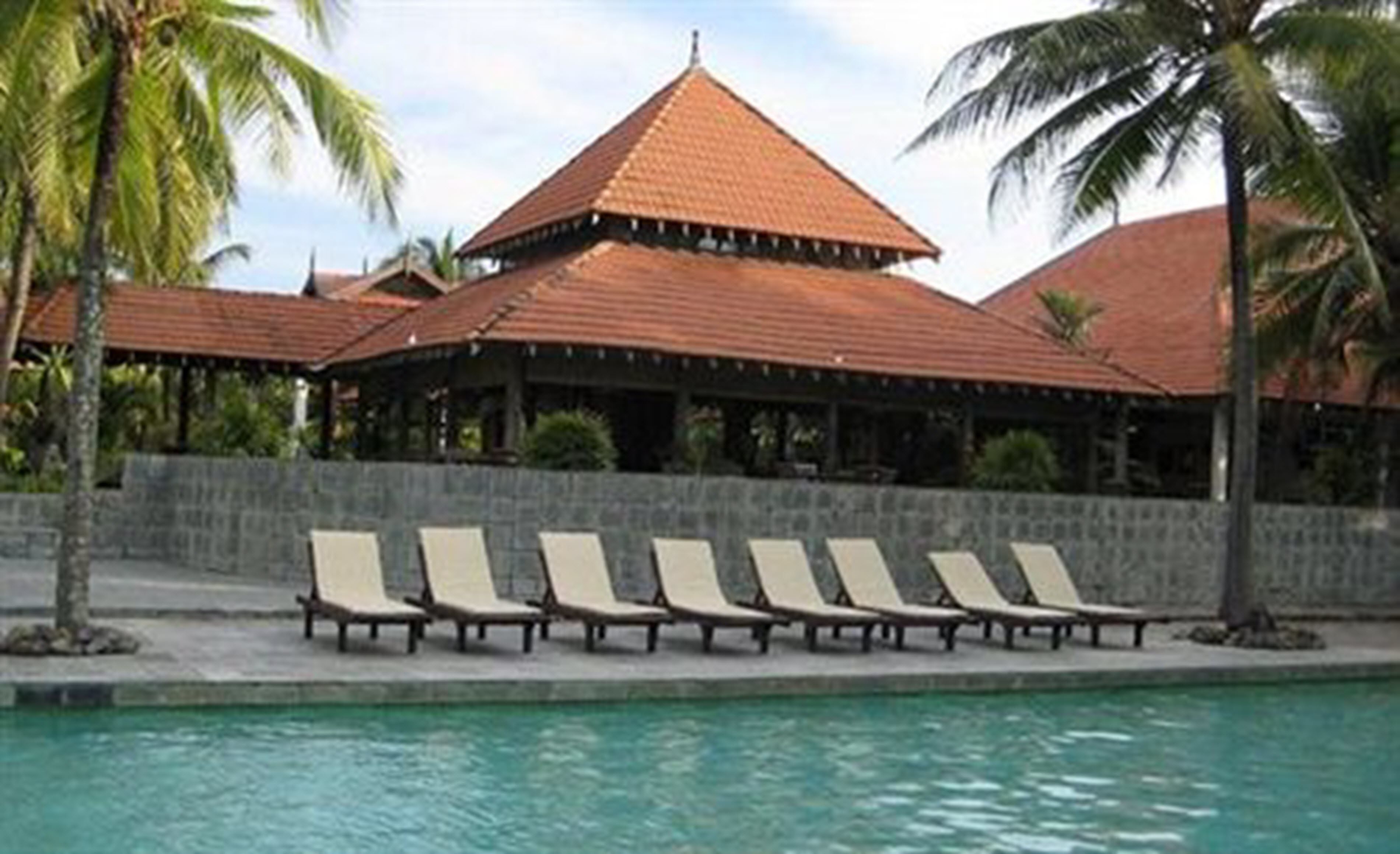 Un espace aménagé au bord de la piscine, avec des chaises longues et un bâtiment doté d’un toit en tuiles.