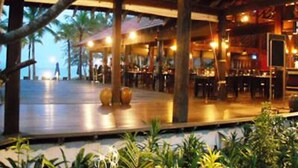 An outdoor dining area with tables and chairs, palm trees, and a covered seating area.