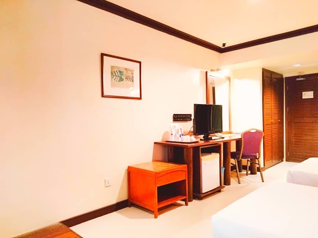 Ein Hotelzimmer mit Bett, Schreibtisch mit Computer, Stuhl, kleinem Tisch, Fernseher und einem gerahmten Bild an der Wand.