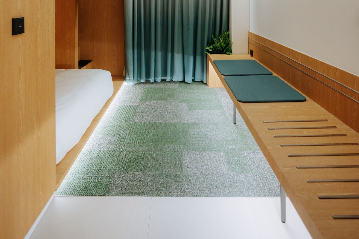 Ein kleines Hotelzimmer mit Etagenbetten, einem kleinen Schreibtisch und einem grünen Teppich.