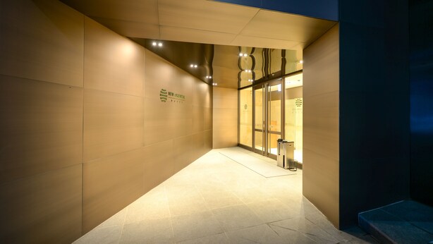 Une entrée d’hôtel moderne, au design épuré et géométrique, avec une enseigne indiquant le nom de l’établissement.