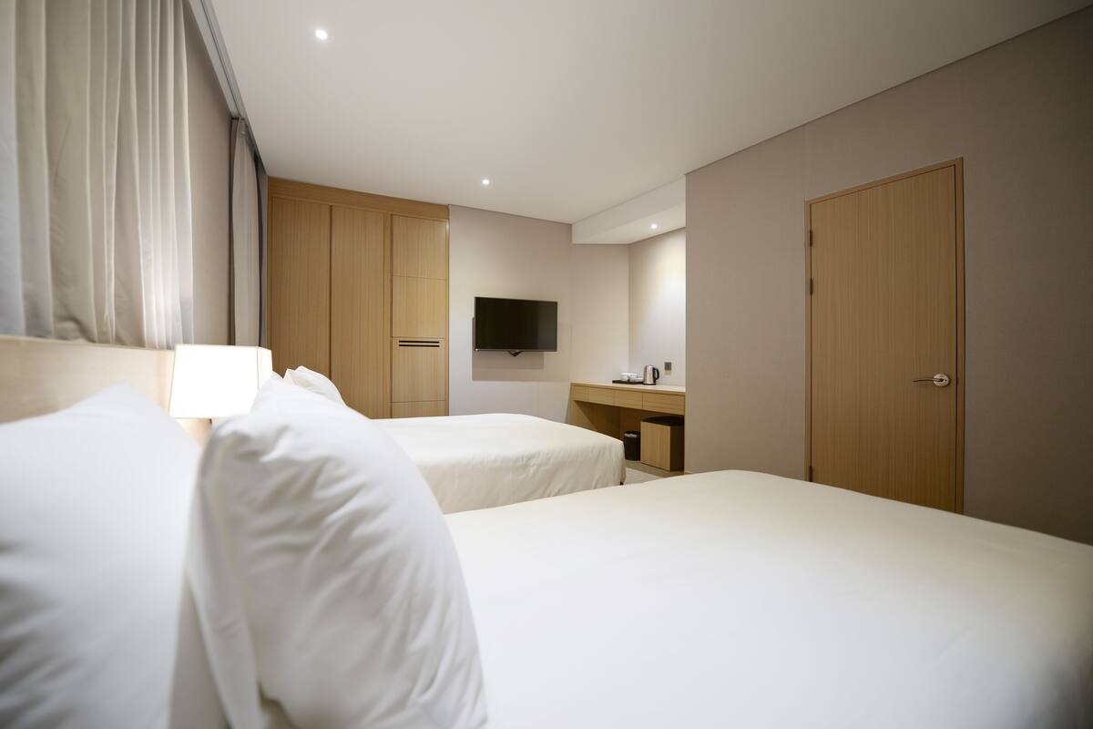 Een hotelkamer met twee bedden, een televisie, een bureau met koffiezetapparaat en houten kasten.
