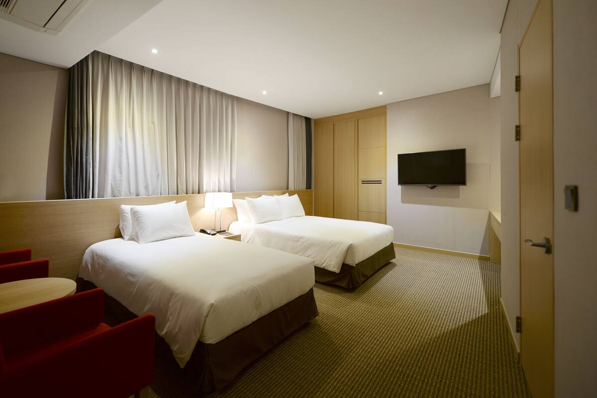 Een hotelkamer met twee bedden, een televisie en een bureau met stoelen.
