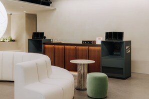 Een modern interieur met een receptiebalie, een witte bank, een klein rond tafeltje en een groene poef.
