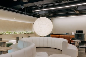 Ein stilvoller Lounge-Bereich mit einer gebogenen weißen Couch, einem runden Tisch und einer außergewöhnlichen Wandleuchte.