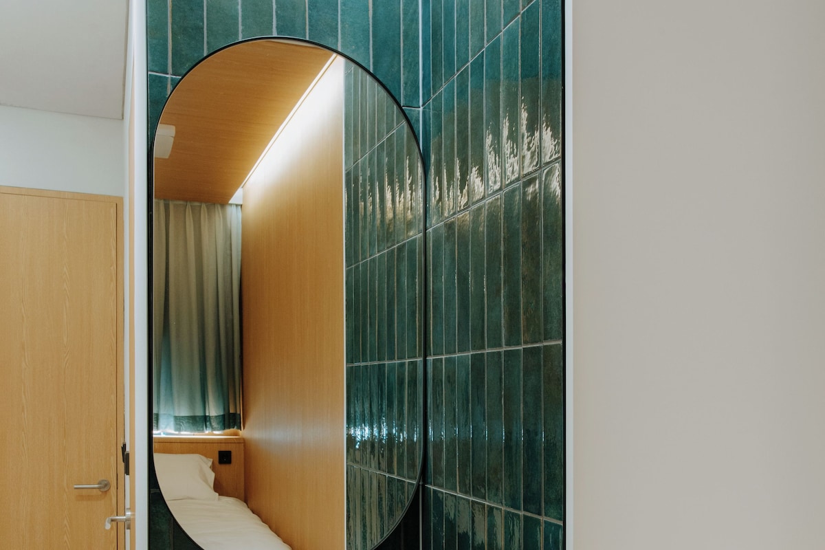 A bathroom with a white sink, a mirror, and green tiled walls.