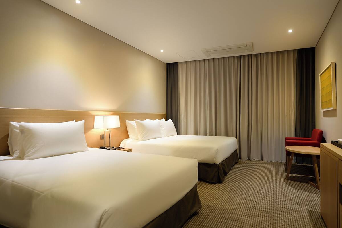 Een hotelkamer met twee bedden, een bureau, een stoel en een groot raam met gordijnen.