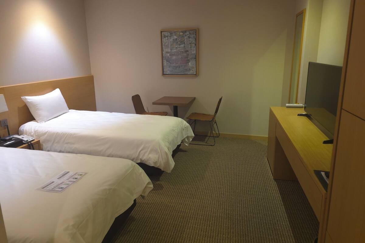 Een hotelkamer met twee bedden, een bureau, een stoel, een televisie en een schilderij aan de muur.