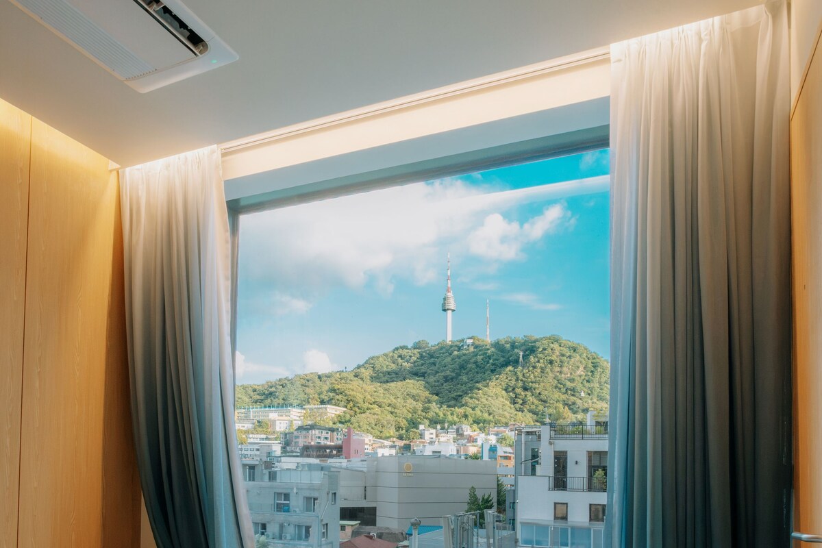 A hotel room with a large window, a view of a cityscape, and a balcony.