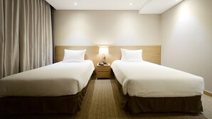Une chambre d’hôtel avec deux lits simples, une table de chevet avec une lampe et une grande fenêtre avec des rideaux.