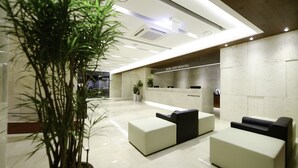 Un hall d’hôtel moderne avec un comptoir d’accueil, un espace salon et une grande plante en pot.