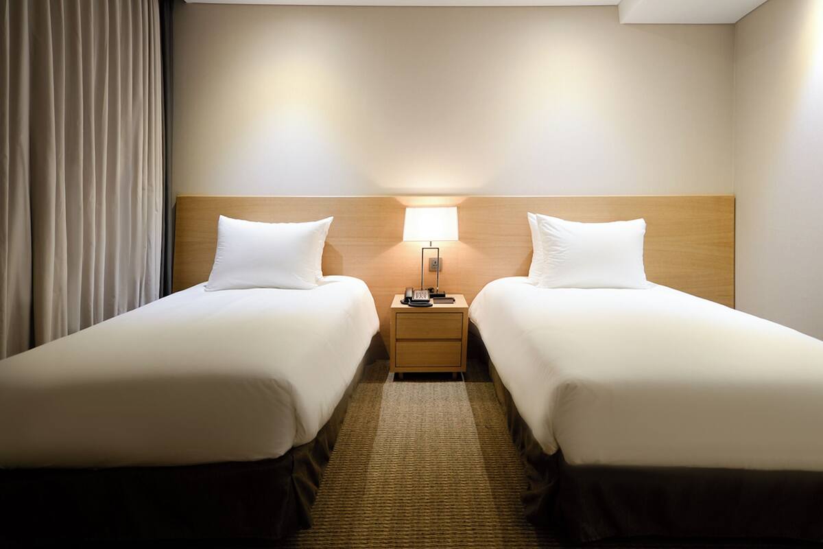 Een hotelkamer met twee eenpersoonsbedden, een nachtkastje met lamp en een groot raam met gordijnen.