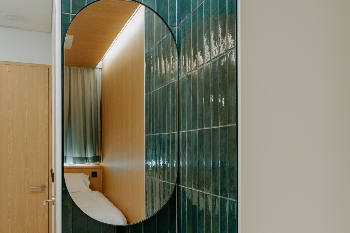Une salle de bain avec un lavabo blanc, un miroir et des murs recouverts de carreaux verts.