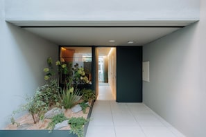 Een moderne ingang met een pad naar een deur, omringd door een kleine tuin met diverse planten en een betegelde vloer.