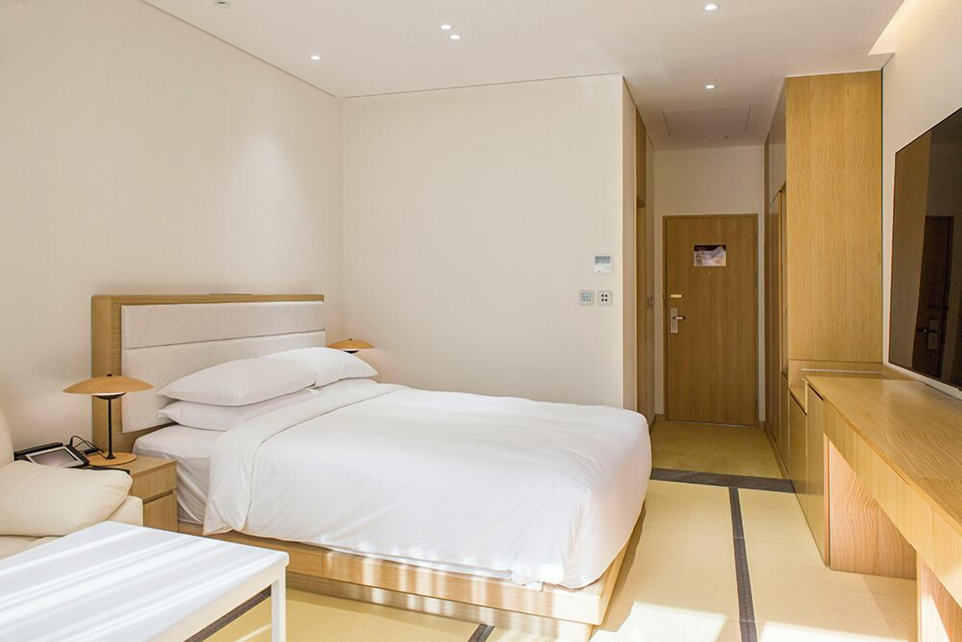 A hotel room with a bed, bedside table, lamp, and a large mirror.