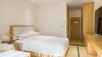 A hotel room with a bed, bedside table, lamp, and a large mirror.