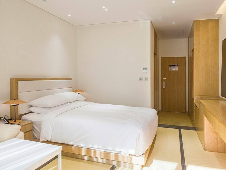 A hotel room with a bed, bedside table, lamp, and a large mirror.