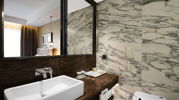 Un baño moderno con un espejo grande, paredes de mármol, un lavamanos blanco y un perchero para toallas.
