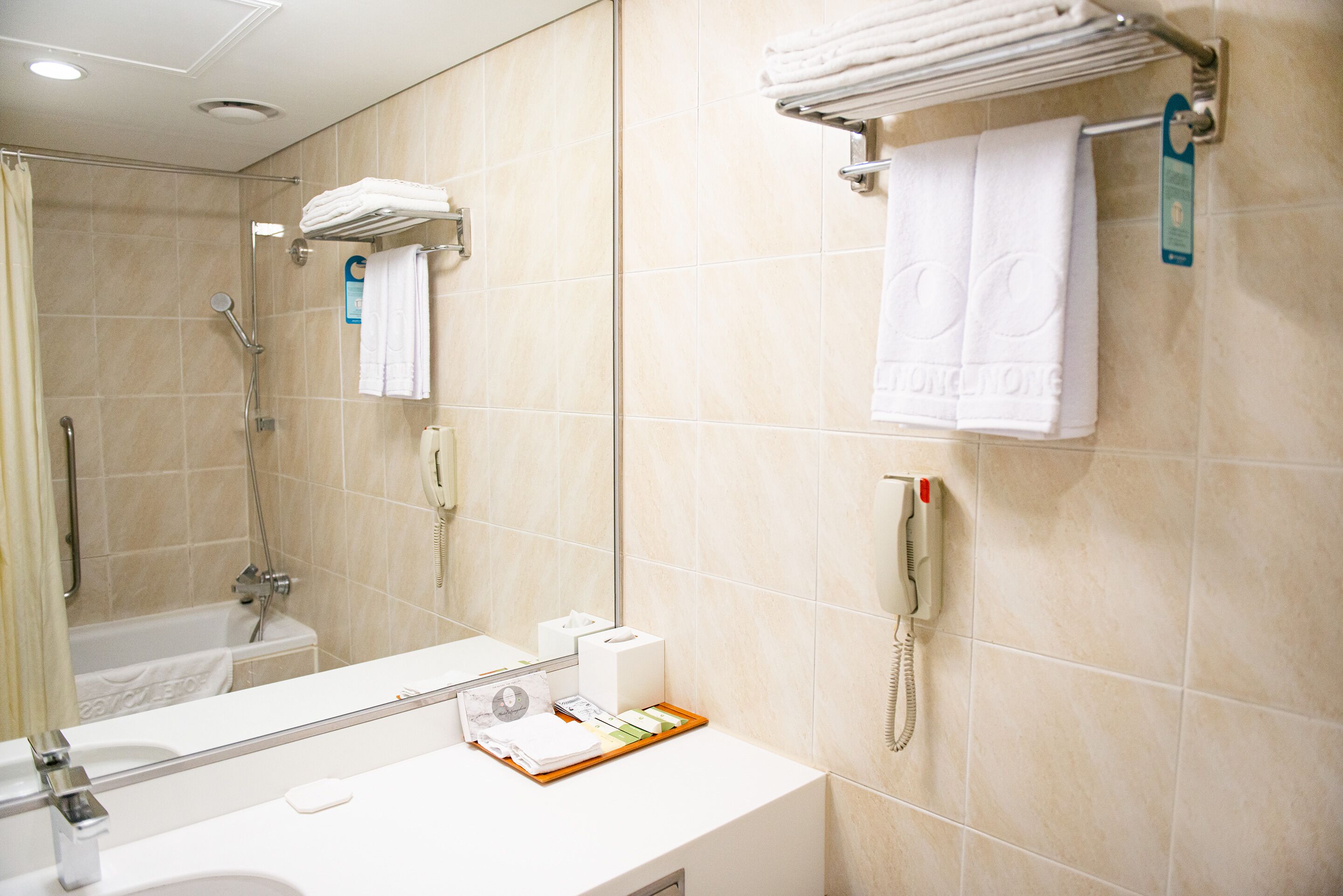 A hotel bathroom with a bathtub, a toilet, a sink, a mirror, a towel rack, and a telephone.