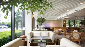 En moderne hotellobby med sofa, stole, et sofabord og et stort vindue med udsigt til gaden.