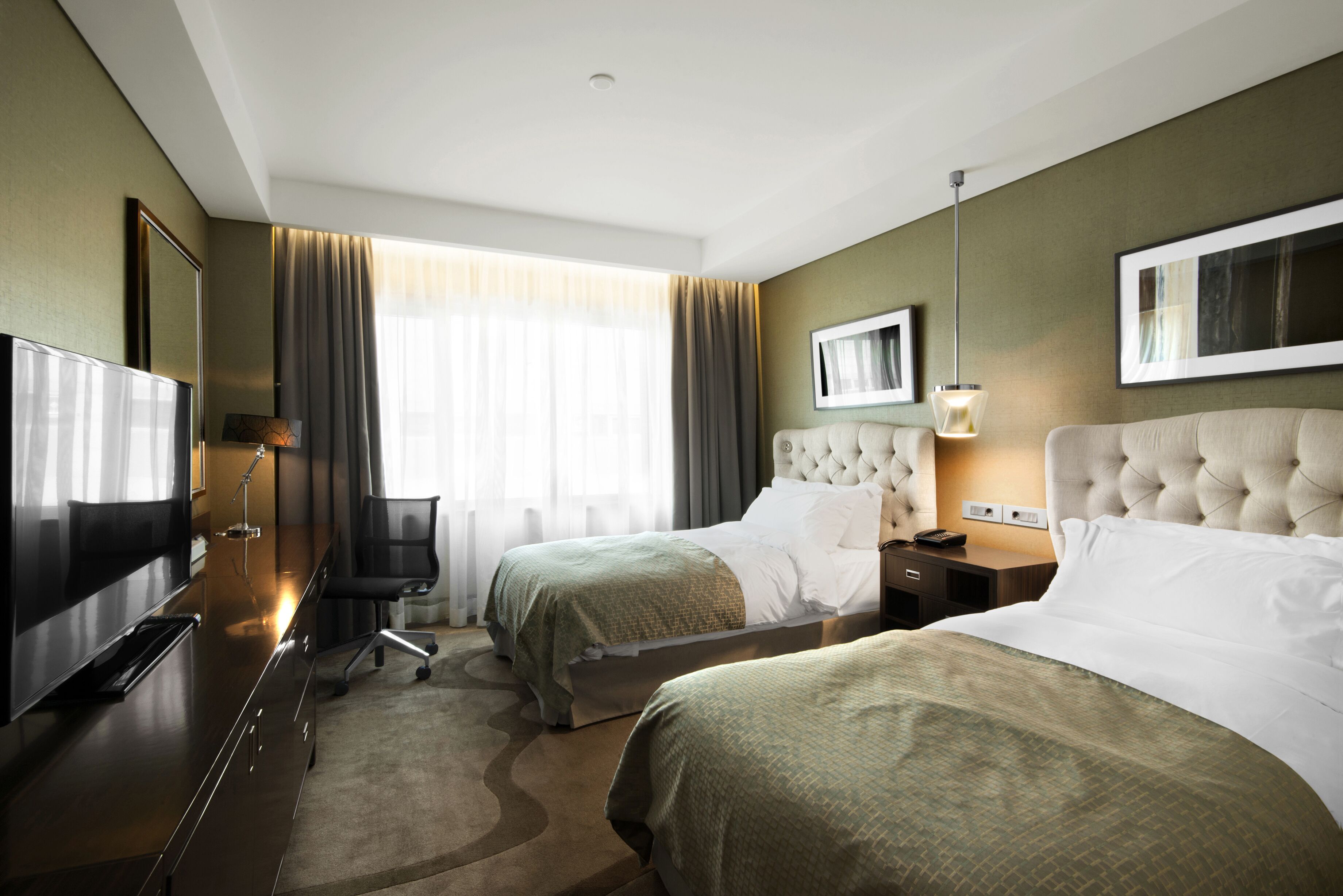 Een hotelkamer met twee bedden, een televisie, een bureau en een groot raam met gordijnen.
