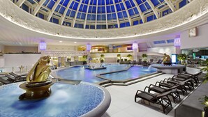 En stor indendørs swimmingpool med glastag, flere siddeområder og dekorative springvand.