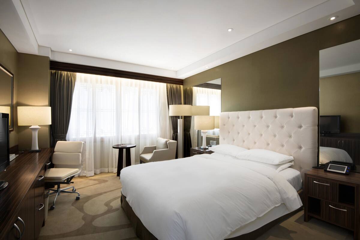 Habitación de hotel con una cama grande, un escritorio con lámpara, dos sillas, un televisor y una mesita de noche.