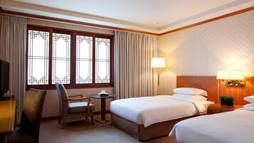 Una habitación de hotel con dos camas, un escritorio con silla, un televisor y una ventana con cortinas.