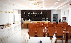 Comedor de hotel con varias mesas y sillas, una zona de bar y una cocina al fondo.