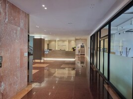 Zona de recepción de un hotel con piso de mármol, mostrador de recepción y pared de vidrio a la derecha.