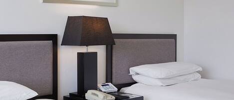 Habitación de hotel con dos camas, una mesita de noche con lámpara, teléfono y un cuadro abstracto enmarcado en la pared.