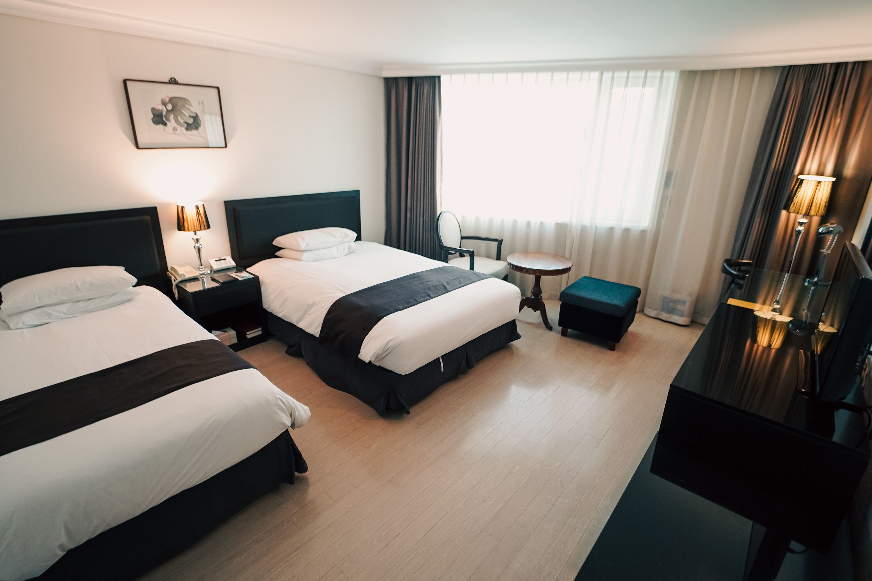 Una habitación de hotel con dos camas, un escritorio, una silla, una mesita y una lámpara.
