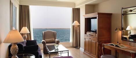 A hotel room with a sofa, armchair, dining table, and a TV.