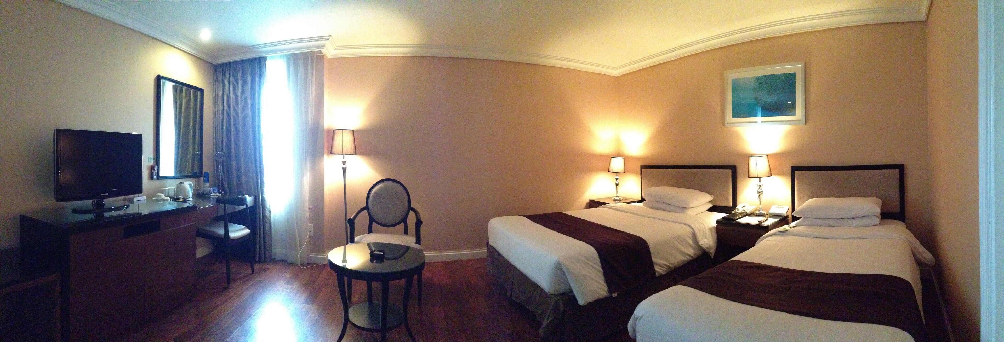 A hotel room with two beds, a desk with a TV, a chair, and two bedside lamps.