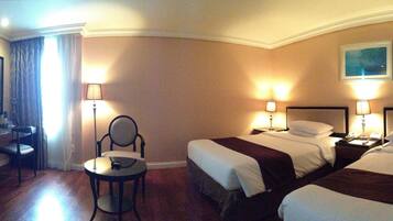 A hotel room with two beds, a desk with a TV, a chair, and two bedside lamps.