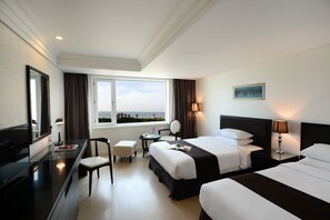 A hotel room with two beds, a desk, a chair, a TV, and a window with a view.