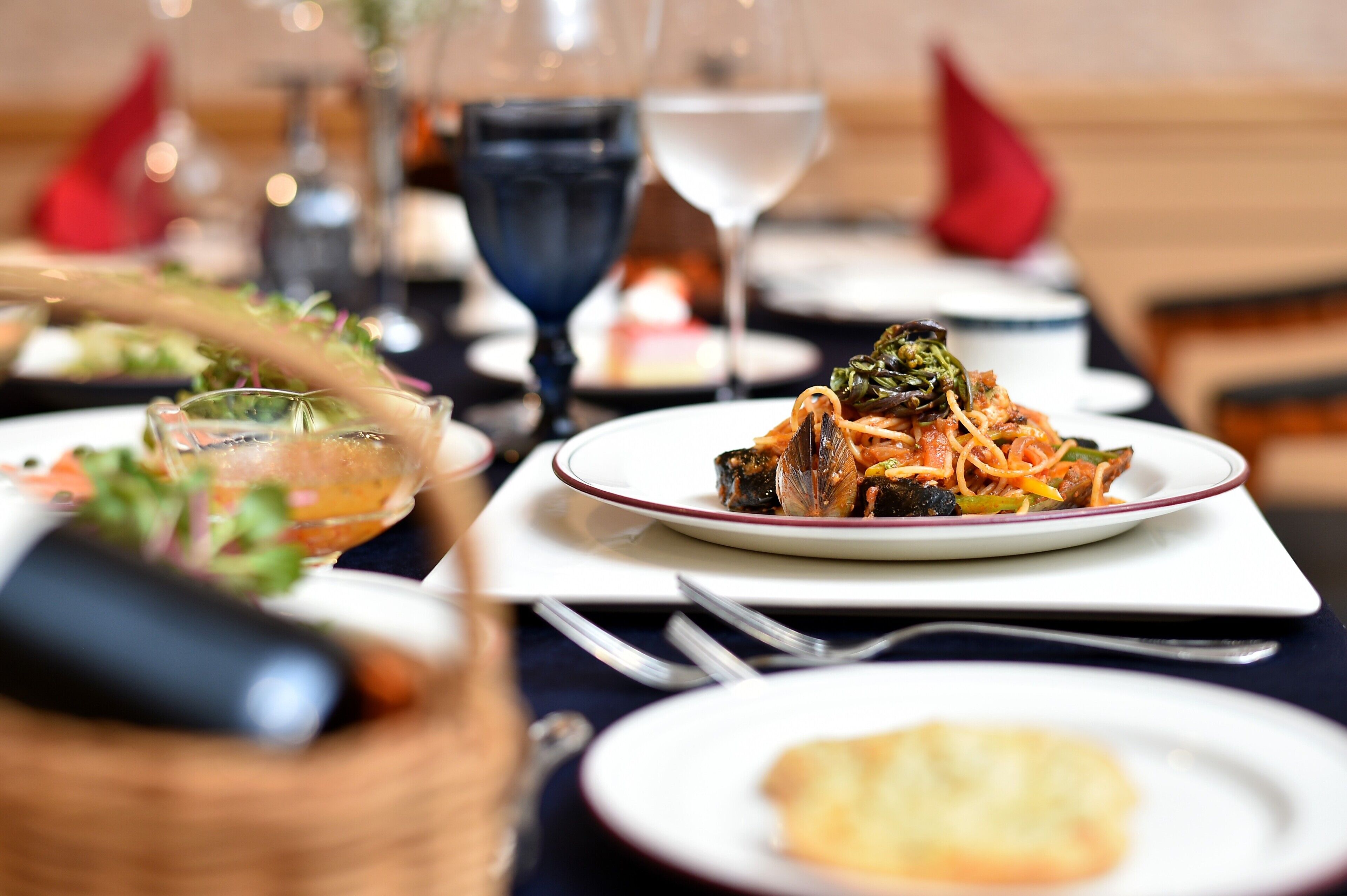 A dining table with plates of food, wine glasses, and cutlery.