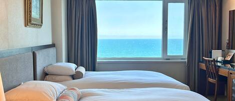 Une chambre d’hôtel avec deux lits, un bureau et une vue sur la mer.