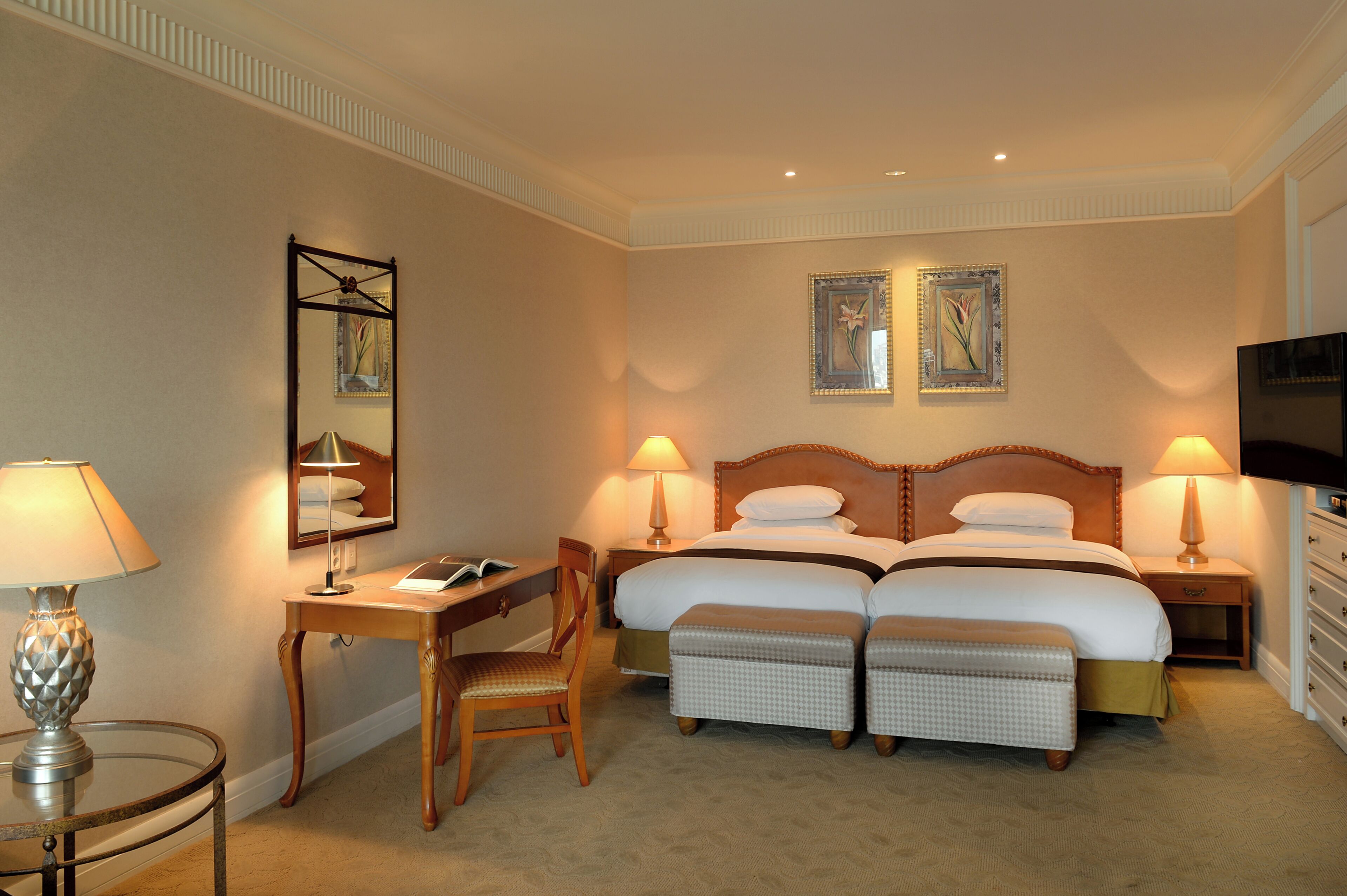Habitación de hotel con cama doble, dos mesitas de noche con lámparas, un escritorio con silla, televisor y dos cuadros en la pared.
