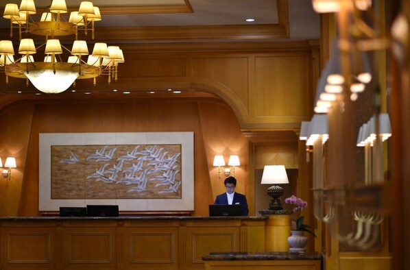 A reception desk with a large abstract painting, a chandelier, and a receptionist.