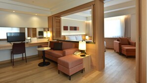 Habitación de hotel con sofá, reposapiés, televisor y escritorio con silla.