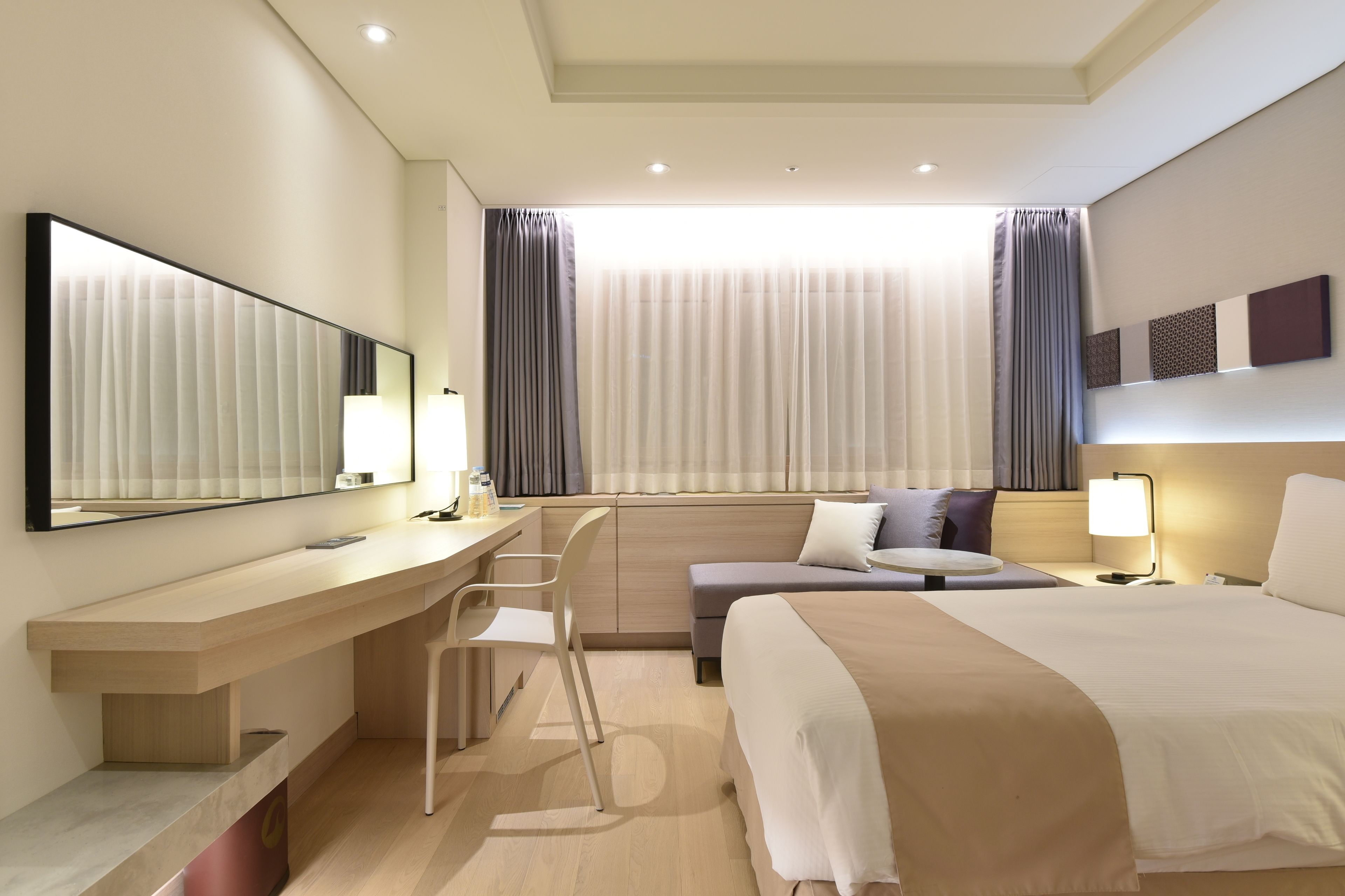 Habitación de hotel moderna con una cama grande, un escritorio con silla, una mesita pequeña y un espejo amplio.