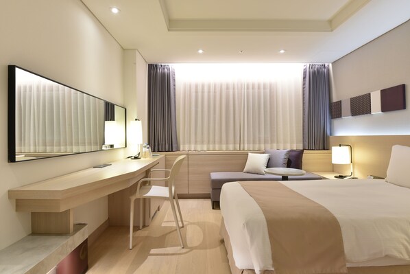 Een moderne hotelkamer met een groot bed, een bureau met stoel, een klein tafeltje en een grote spiegel.