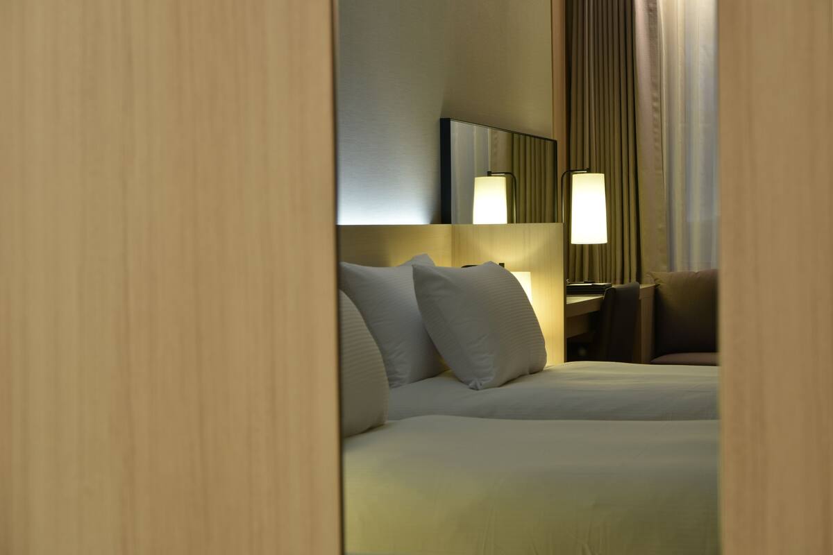 A hotel room with a bed, a desk, a chair, a lamp, and a mirror.