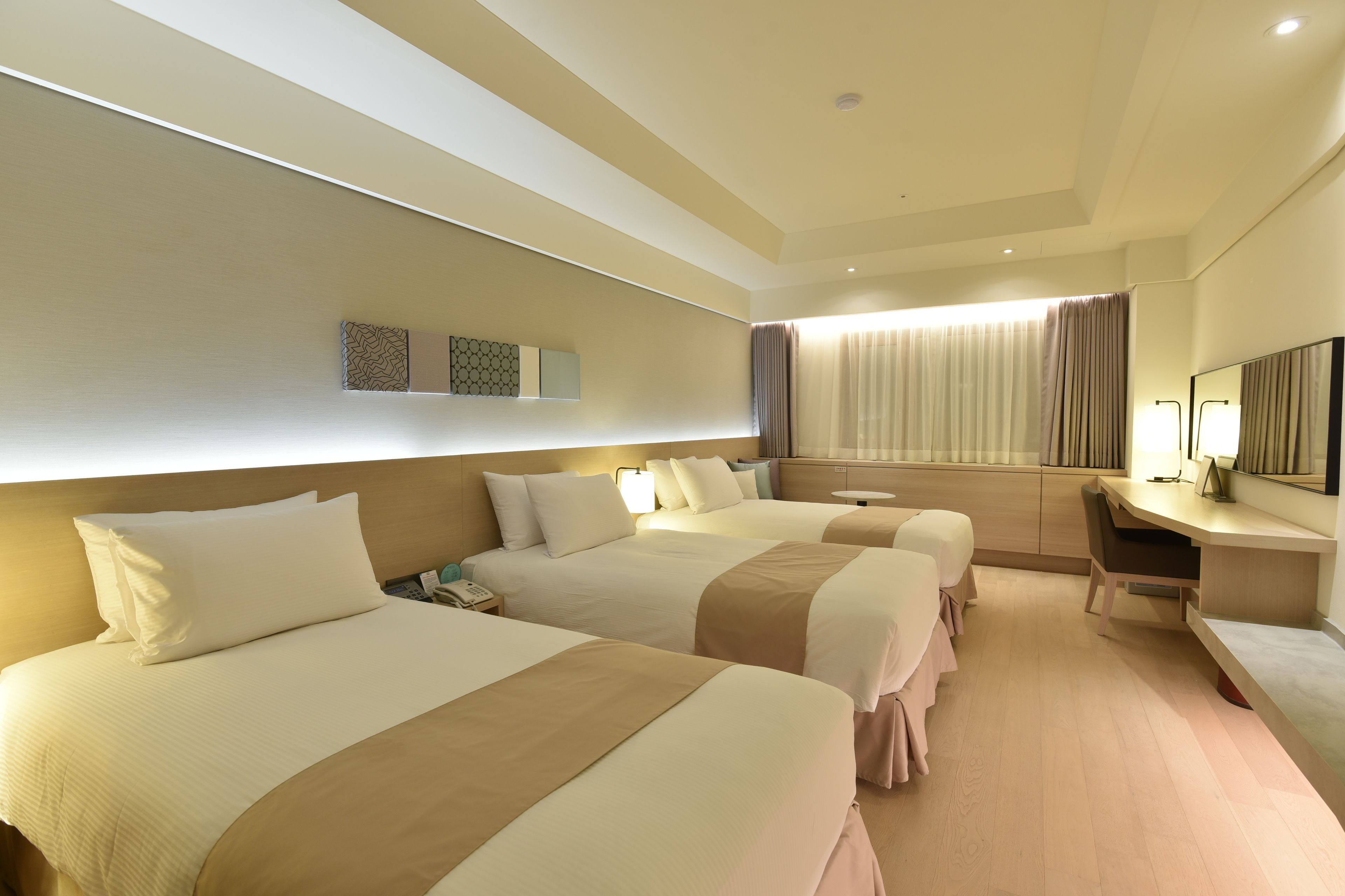 A hotel room with three beds, a desk, a chair, and a large mirror.