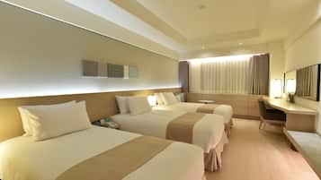 A hotel room with three beds, a desk, a chair, and a large mirror.