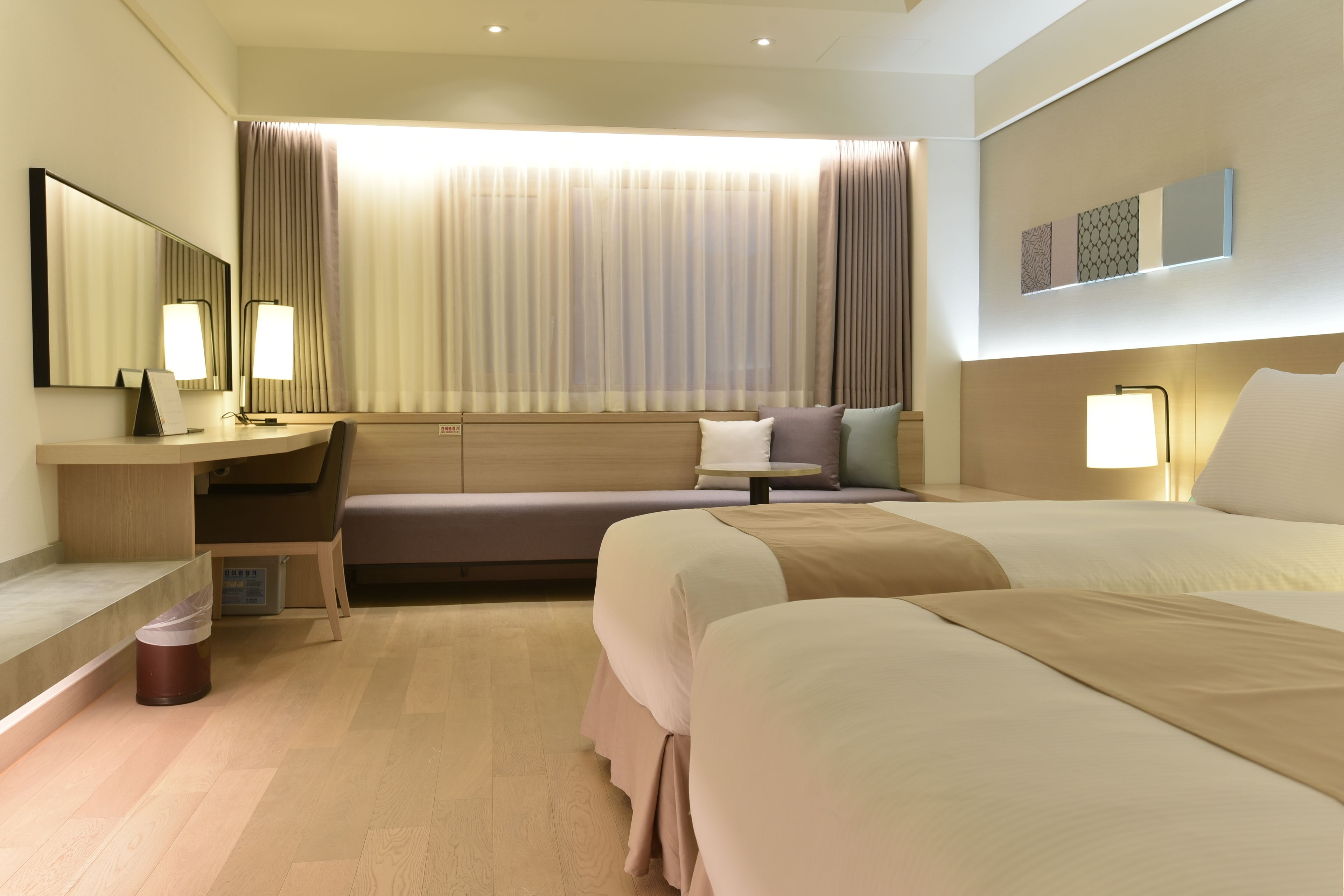 Una habitación de hotel moderna con una cama grande, un escritorio con silla, un sofá y un ventanal con cortinas.