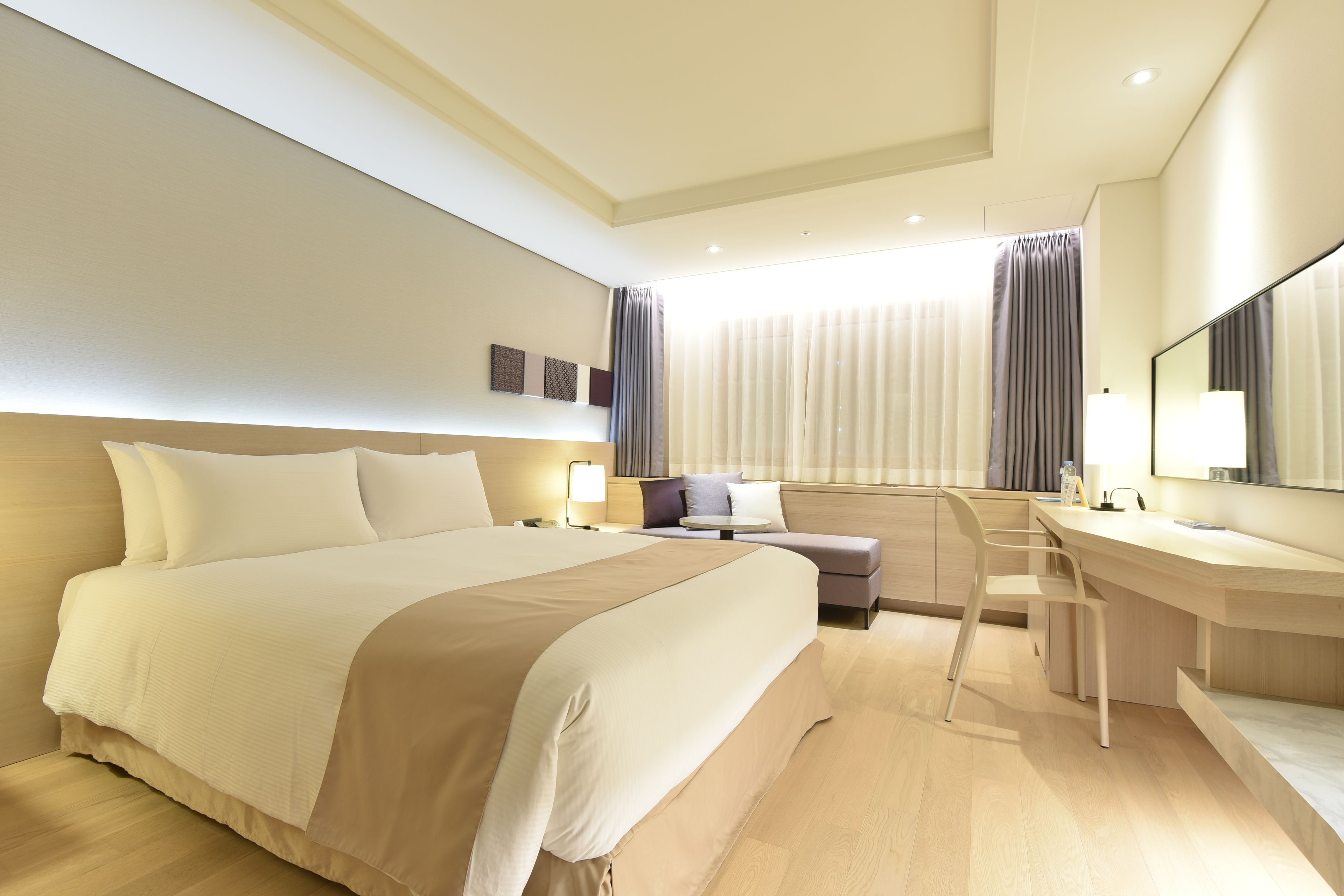 A modern hotel room with a large bed, a desk, and a chair.