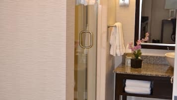 Une salle de bain dotée d’une douche à parois de verre, d’un lavabo avec un plan de travail en marbre et d’un miroir au-dessus du lavabo.